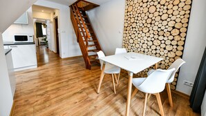 A dining area with a white table and chairs, a wooden staircase, and a wall of stacked logs. - Rentplanet - Bulwary Słowackiego (Zakopane)