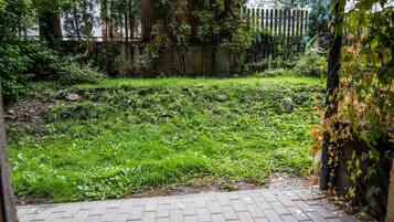 Uma área de pátio externa com piso de tijolos e vista para uma área gramada com árvores e uma cerca ao fundo.