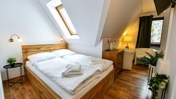 Quarto moderno com cama de madeira, clarabóia, mesa de cabeceira com luminária, cadeira e planta em vaso.