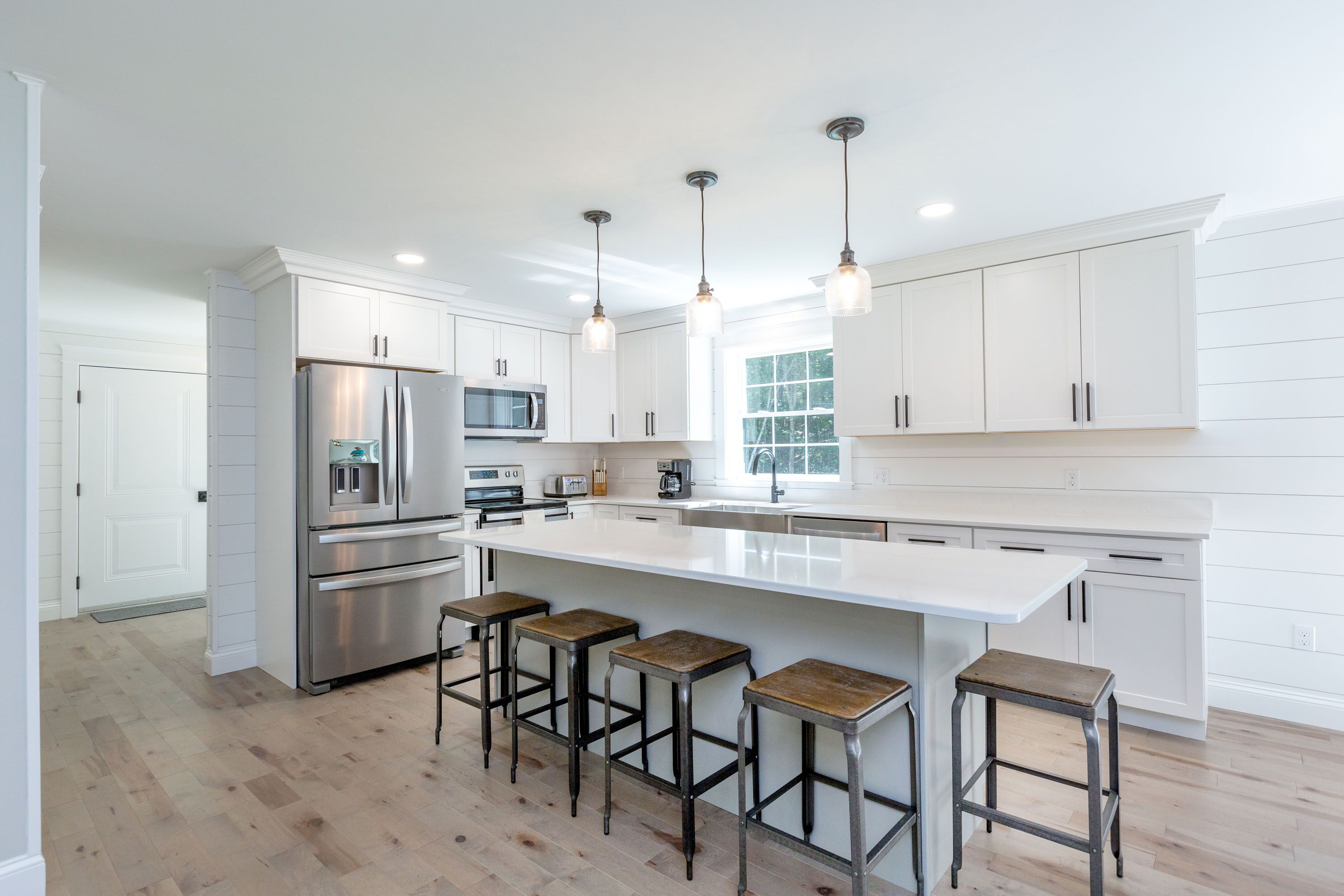A modern kitchen with white cabinetry, stainless steel appliances, and a central island with bar stools.