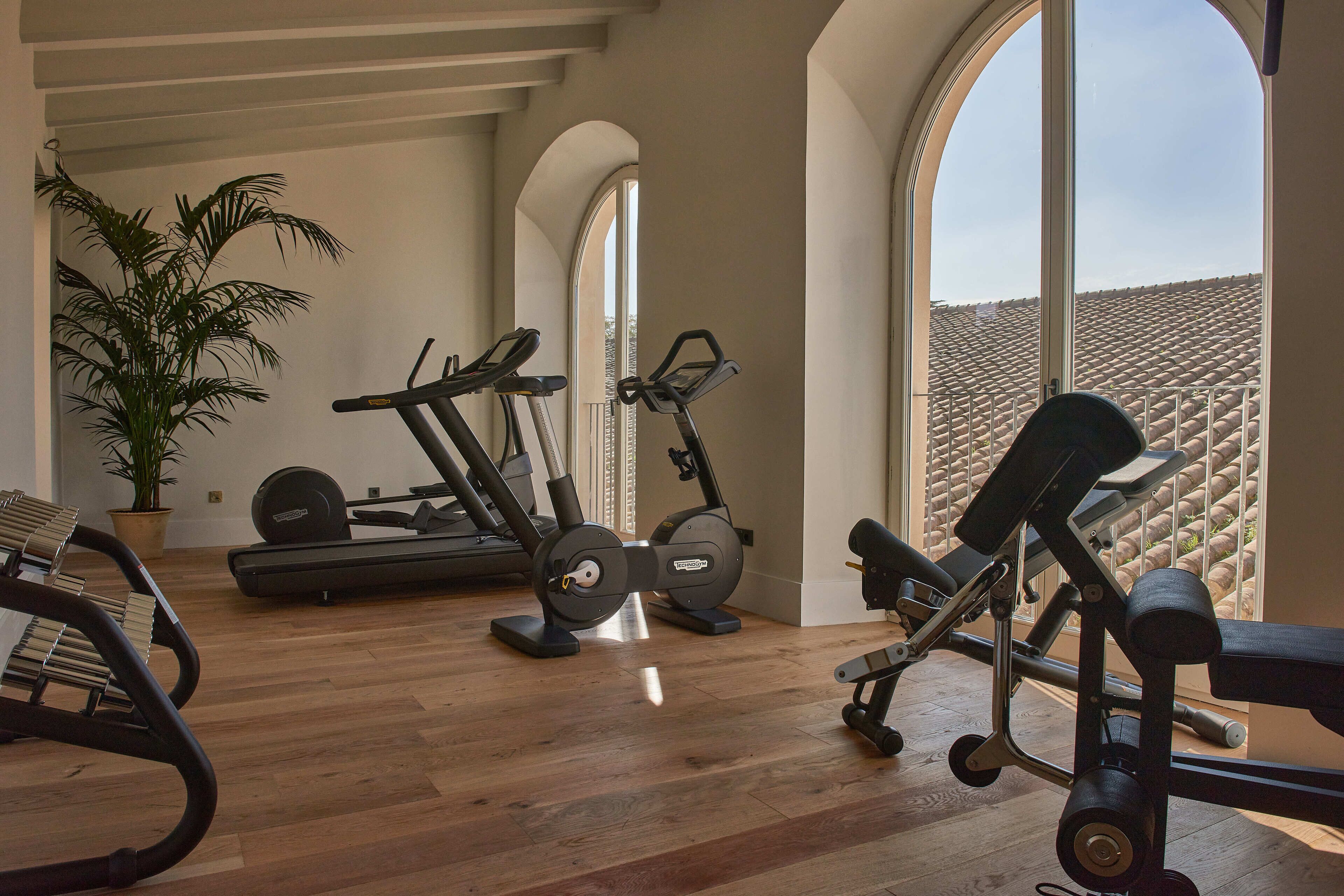 A spacious home gym with exercise equipment, large windows, and a wooden floor.