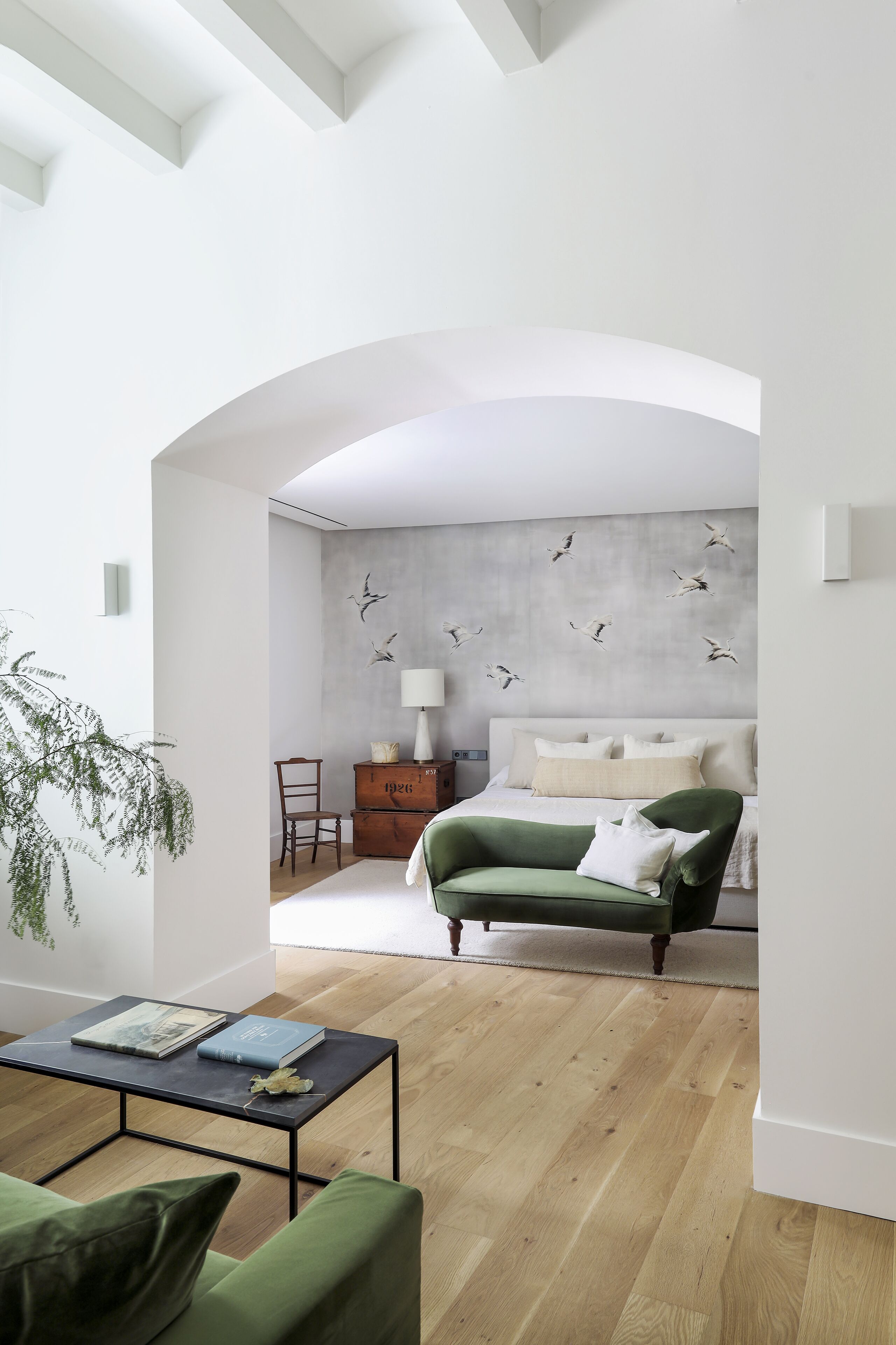 A modern living room with a green sofa, a wooden coffee table, and a bed with a grey concrete wall and bird decals.