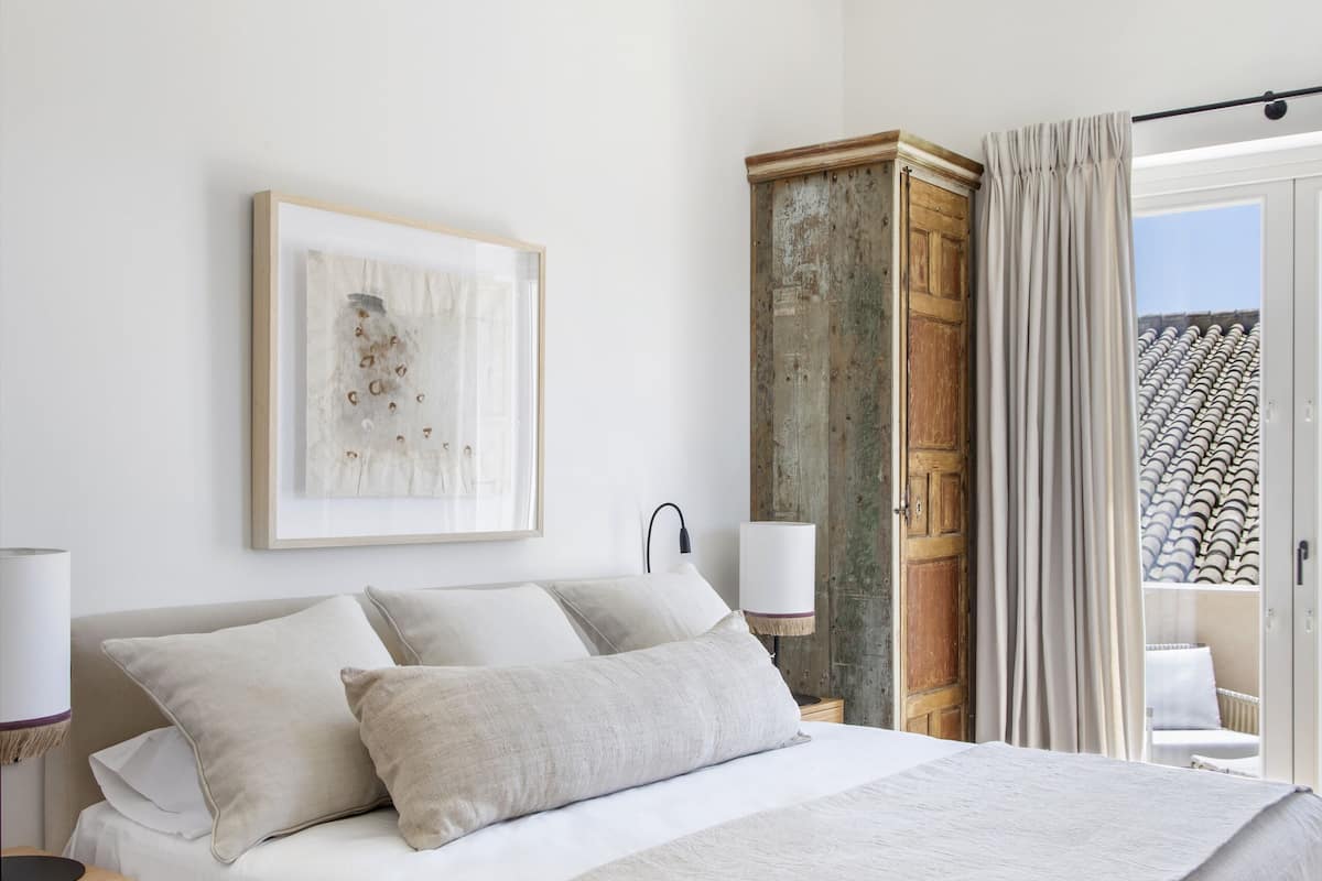 Une chambre à coucher avec un lit, une table de chevet, une lampe, une armoire et une vue sur l’extérieur.