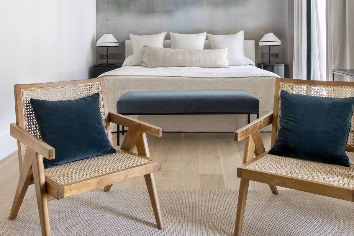 Une chambre avec un grand lit, deux chaises en bois avec des coussins, une fresque murale représentant des oiseaux et une table de chevet avec une lampe.