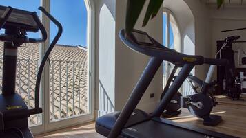 A gym with exercise equipment, large windows, and a view of a tiled roof outside.