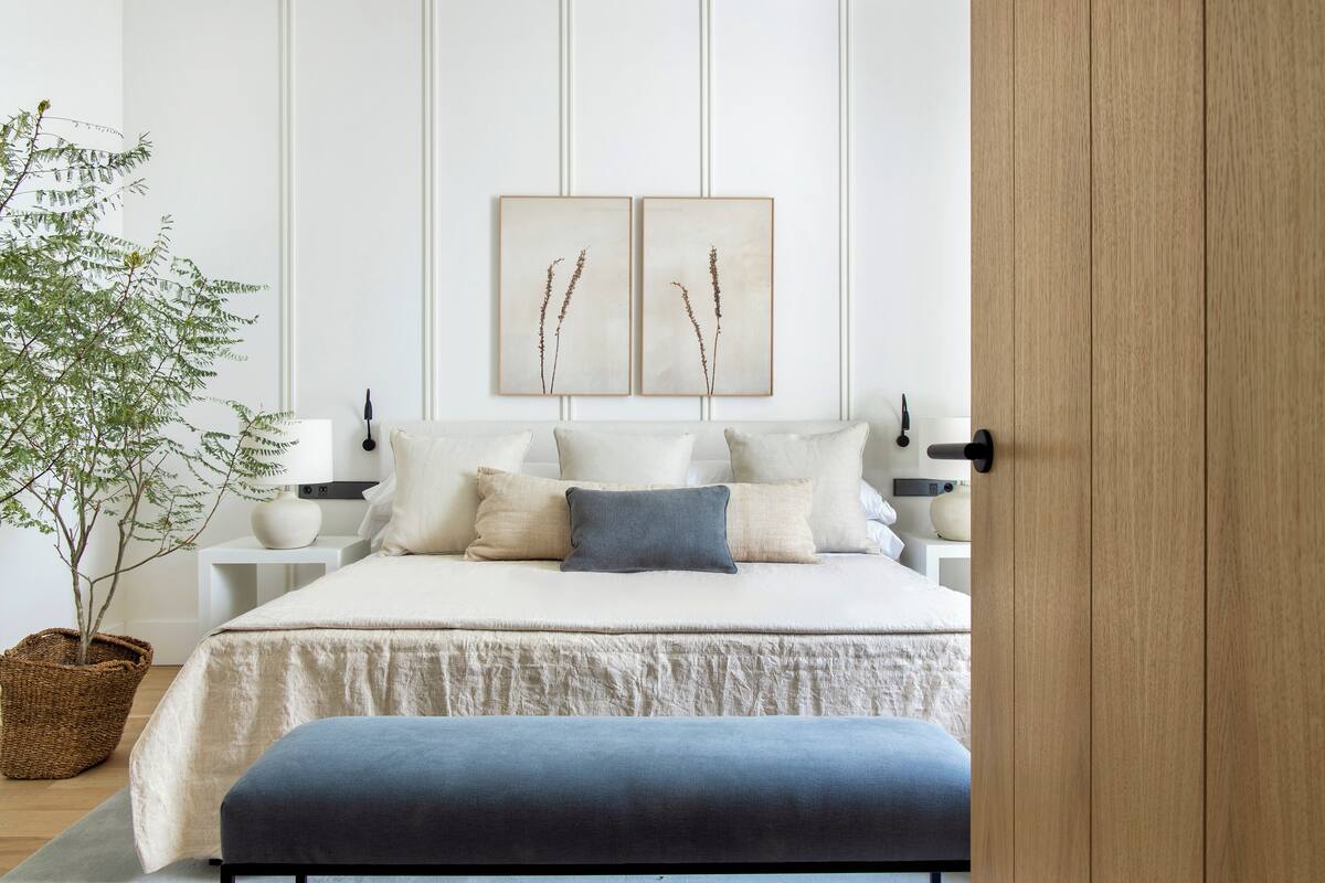 Une chambre à coucher avec un lit, des oreillers, une table de chevet, une lampe et une œuvre d’art accrochée au mur.