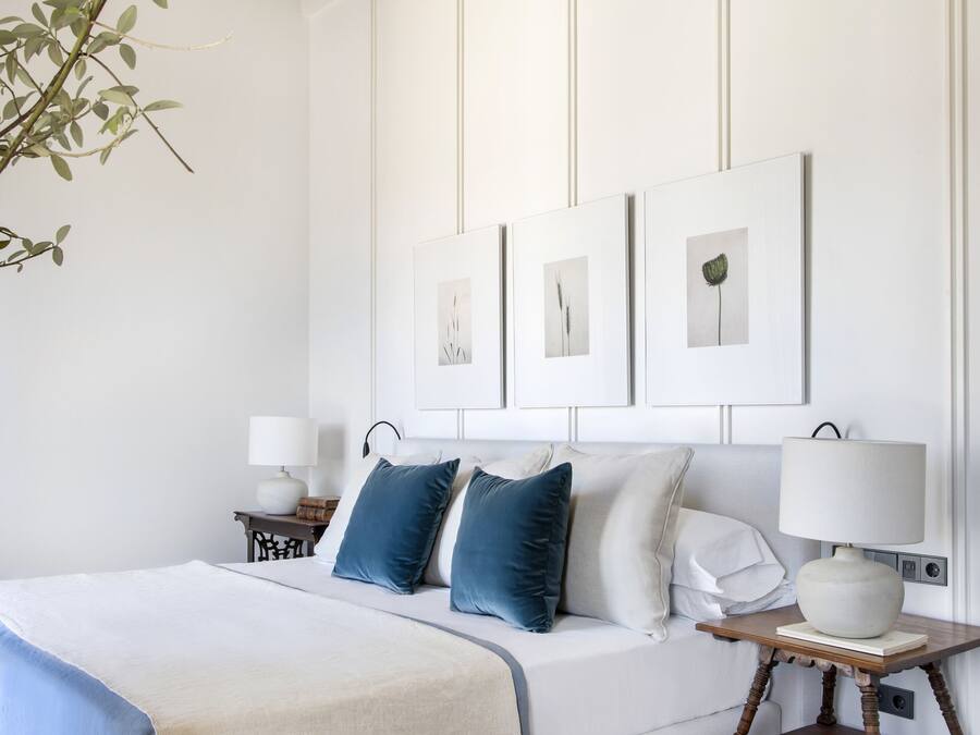 A bedroom with a bed, a blue chair, a wooden table, and wall-mounted lamps.