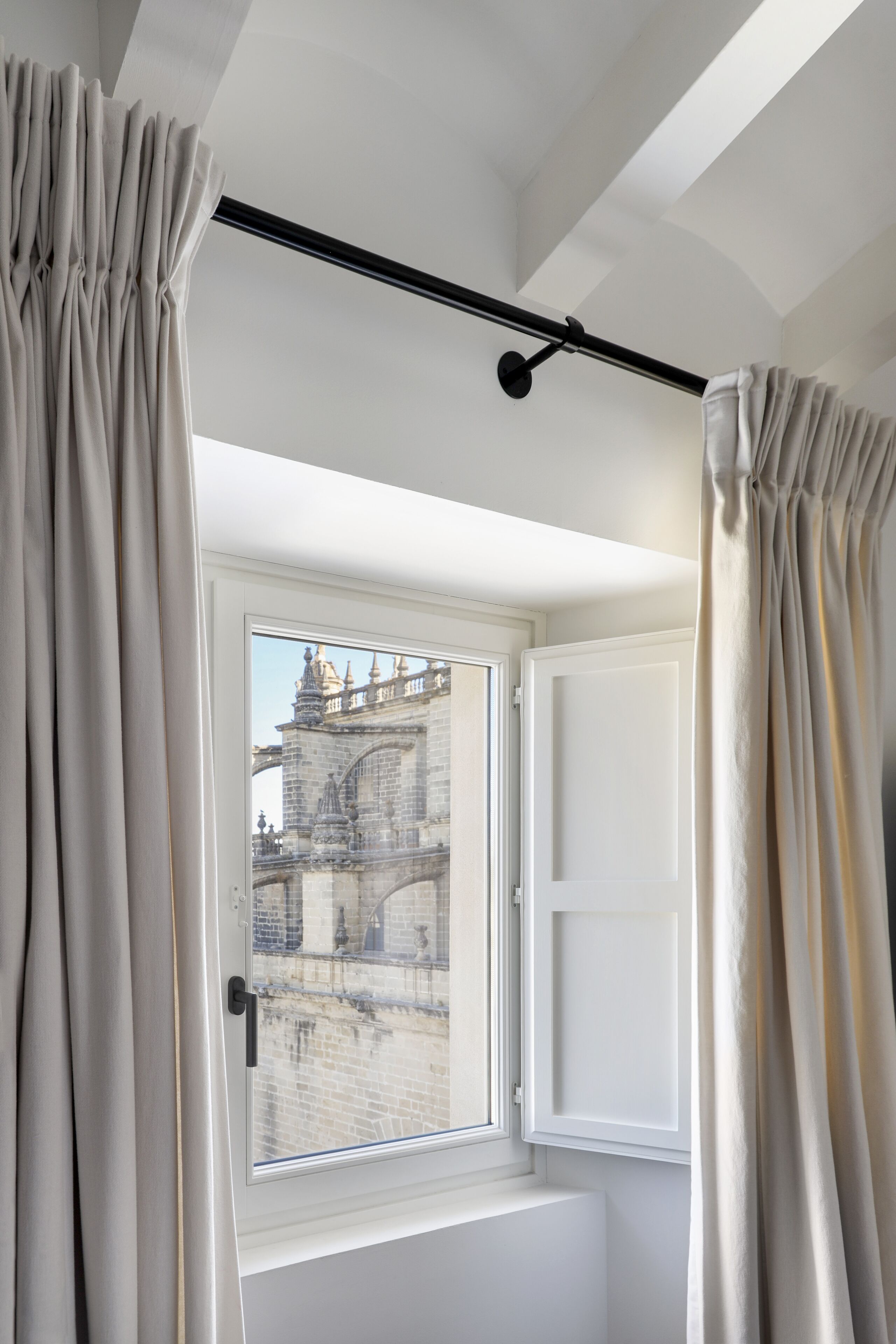 Habitación con ventana que da a un edificio histórico, cortinas en la ventana y techo con vigas a la vista.