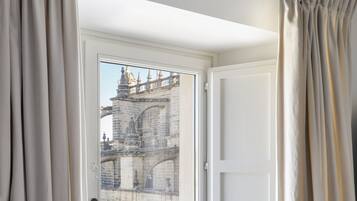 Habitación con ventana que da a un edificio histórico, cortinas en la ventana y techo con vigas a la vista.