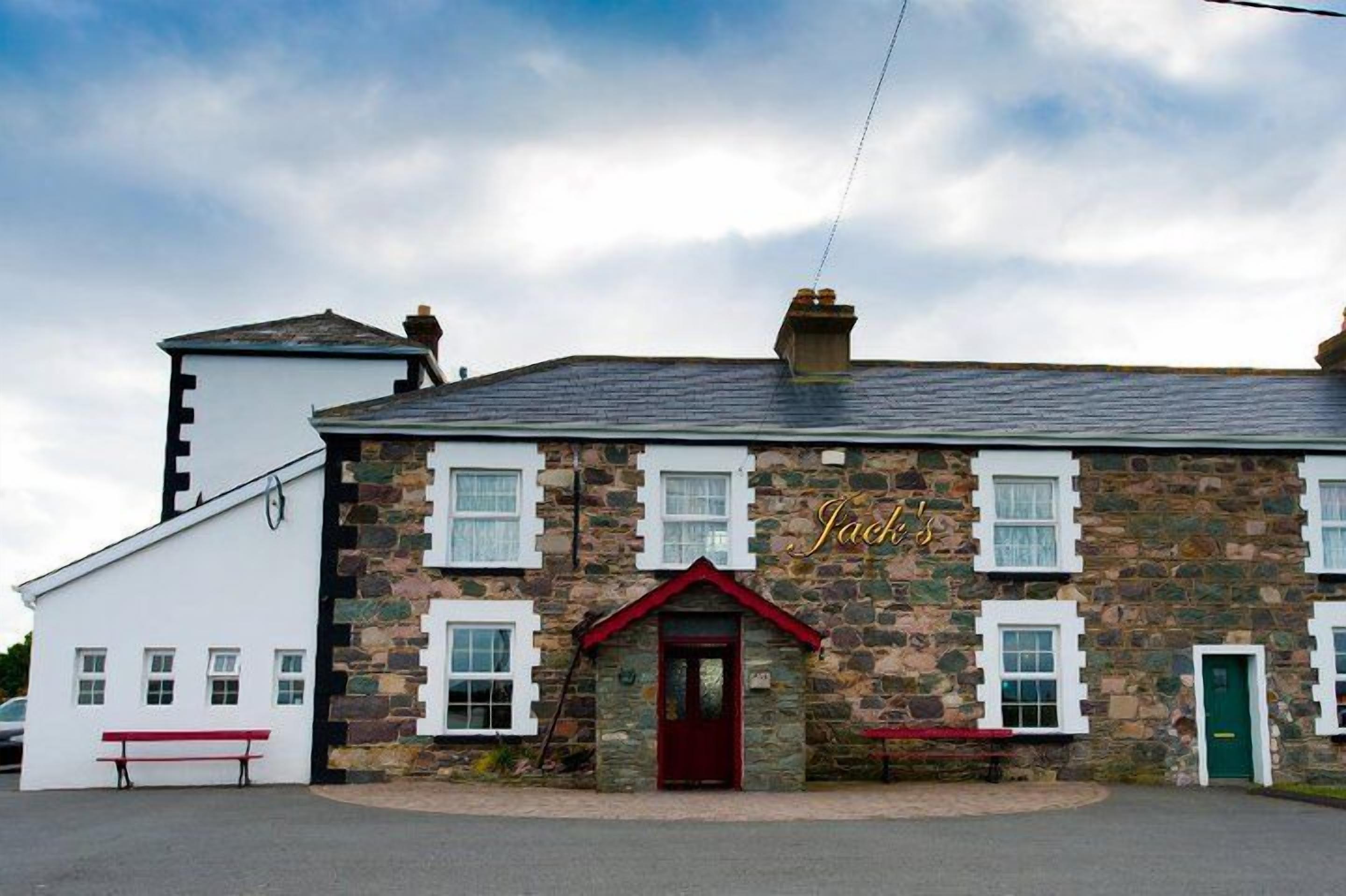 Un edificio de piedra con puerta roja y ventanas enmarcadas en blanco, con la leyenda "Jach's".