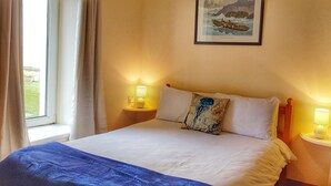 A neatly made bed with white linens, two bedside lamps, a framed picture on the wall, and a window with curtains. - Jacks Coastguard Cottage (Killorglin)