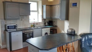 A compact kitchen with a refrigerator, microwave, oven, sink, and a small island with stools. - Jacks Coastguard Cottage (Killorglin)
