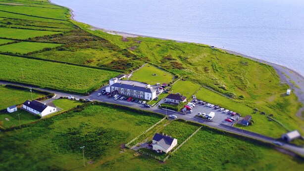 An aerial view of a coastal area with a large building, parking lot, and green fields. - Jacks Coastguard Cottage (Killorglin)