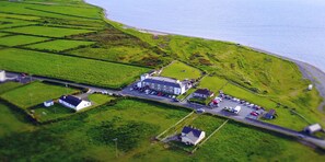 An aerial view of a coastal area with a large building, parking lot, and green fields. - Jacks Coastguard Cottage (Killorglin)