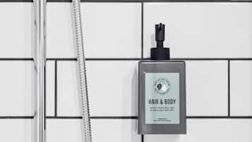 A bathroom with a shower and a bottle of hair and body wash on the wall.