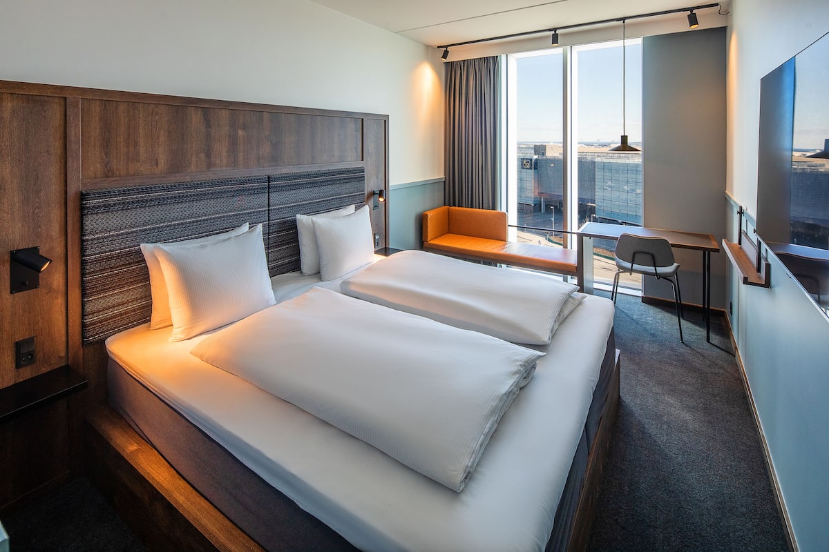 A hotel room with a large bed, a desk, and a view of the city.