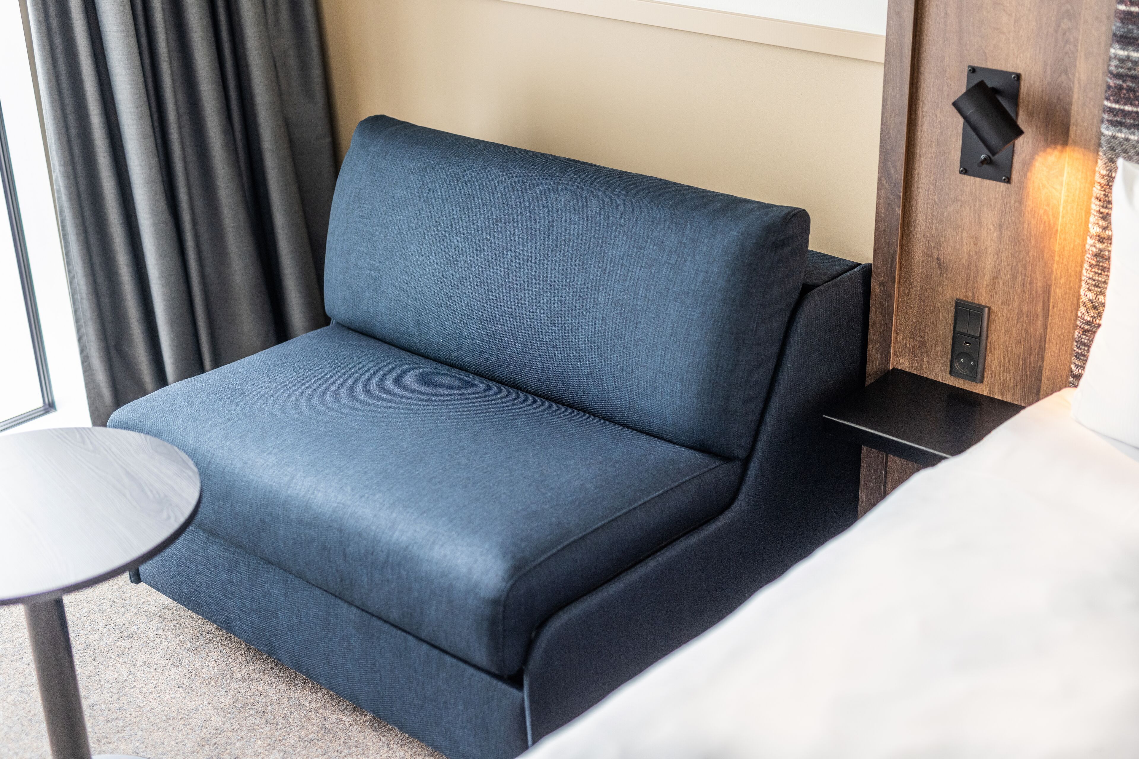 Et moderne værelse med en blå sofa, et lille rundt bord og en trævæg med en lampe.