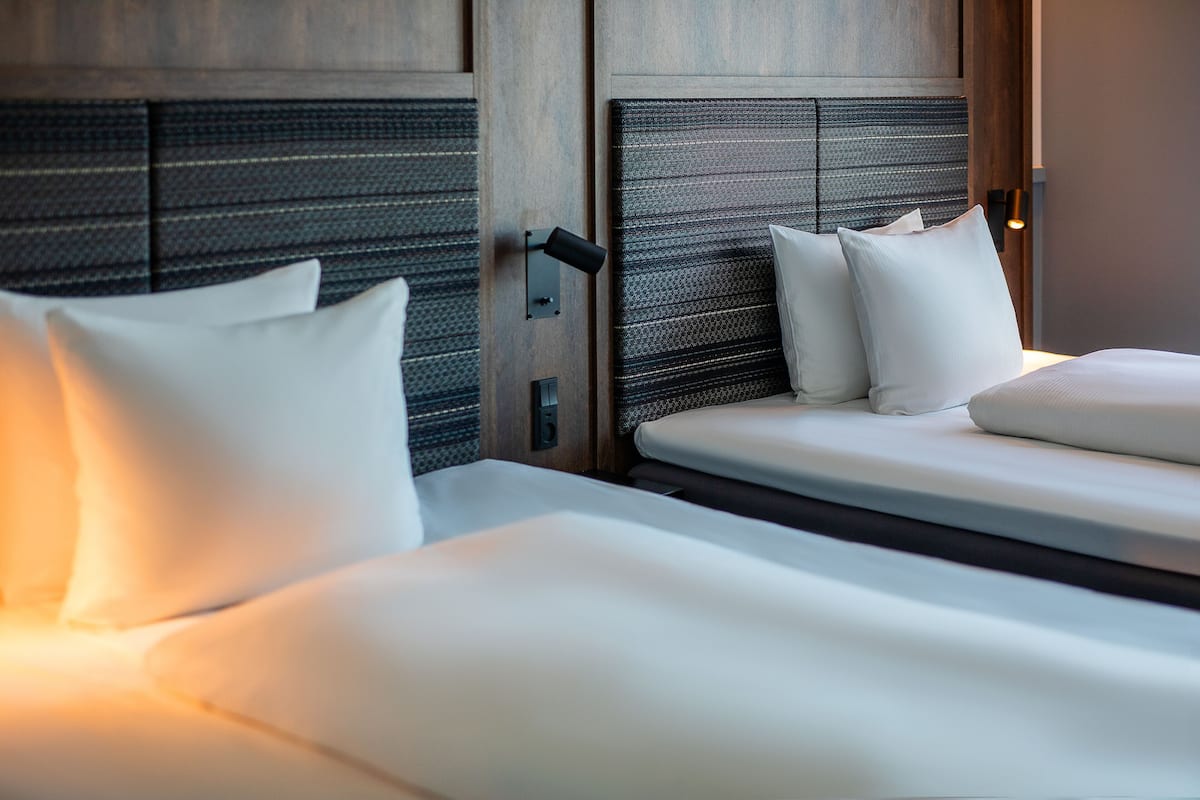 A hotel room with two beds, each with white linens and pillows, and a textured headboard.