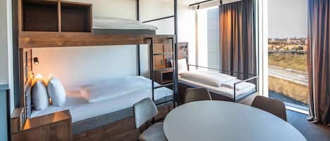 Habitación de hotel pequeña con literas, un escritorio, una mesa redonda y vistas al exterior.