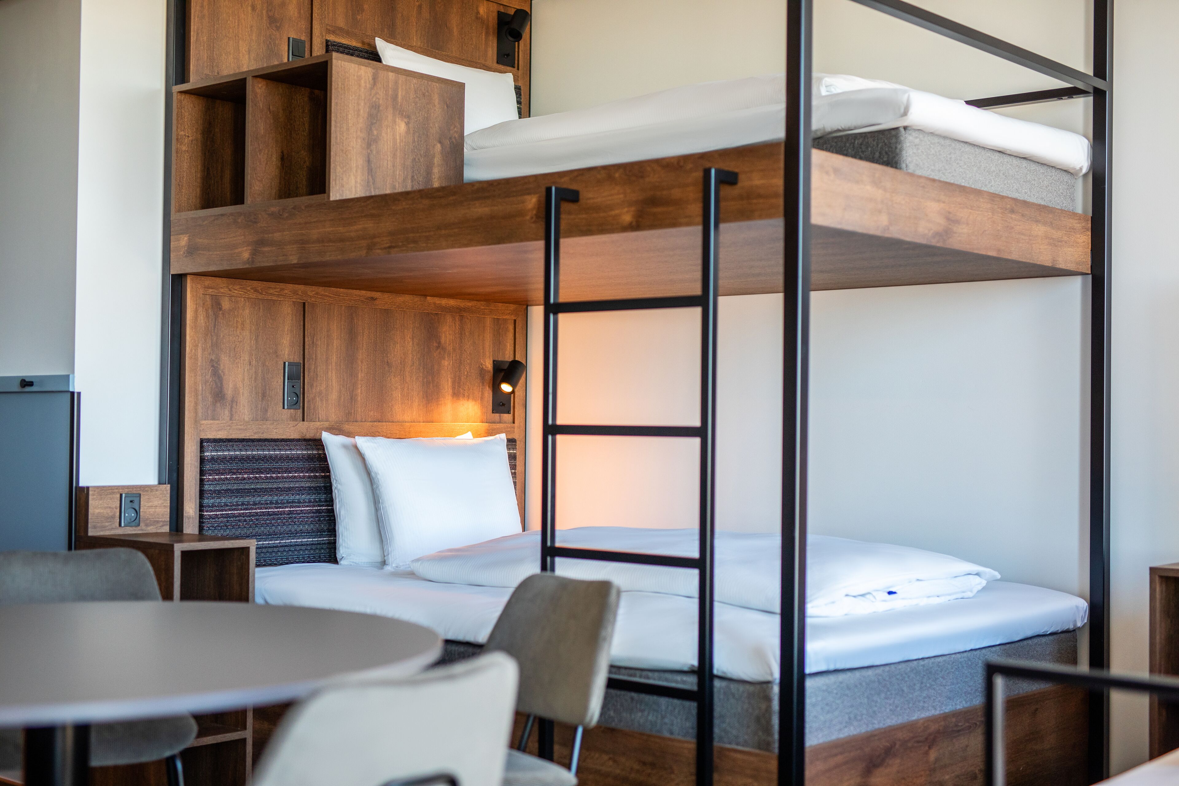 Une chambre avec un lit superposé, un bureau et une chaise, des armoires en bois et une petite table.