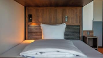 A neatly made bed with a white comforter and pillows, a wooden headboard, and a small bedside table with a lamp.