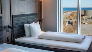 A hotel room with a large bed, a headboard with a textured panel, and a view of the cityscape and water through the window. - Comfort Hotel Copenhagen Airport (Kastrup)