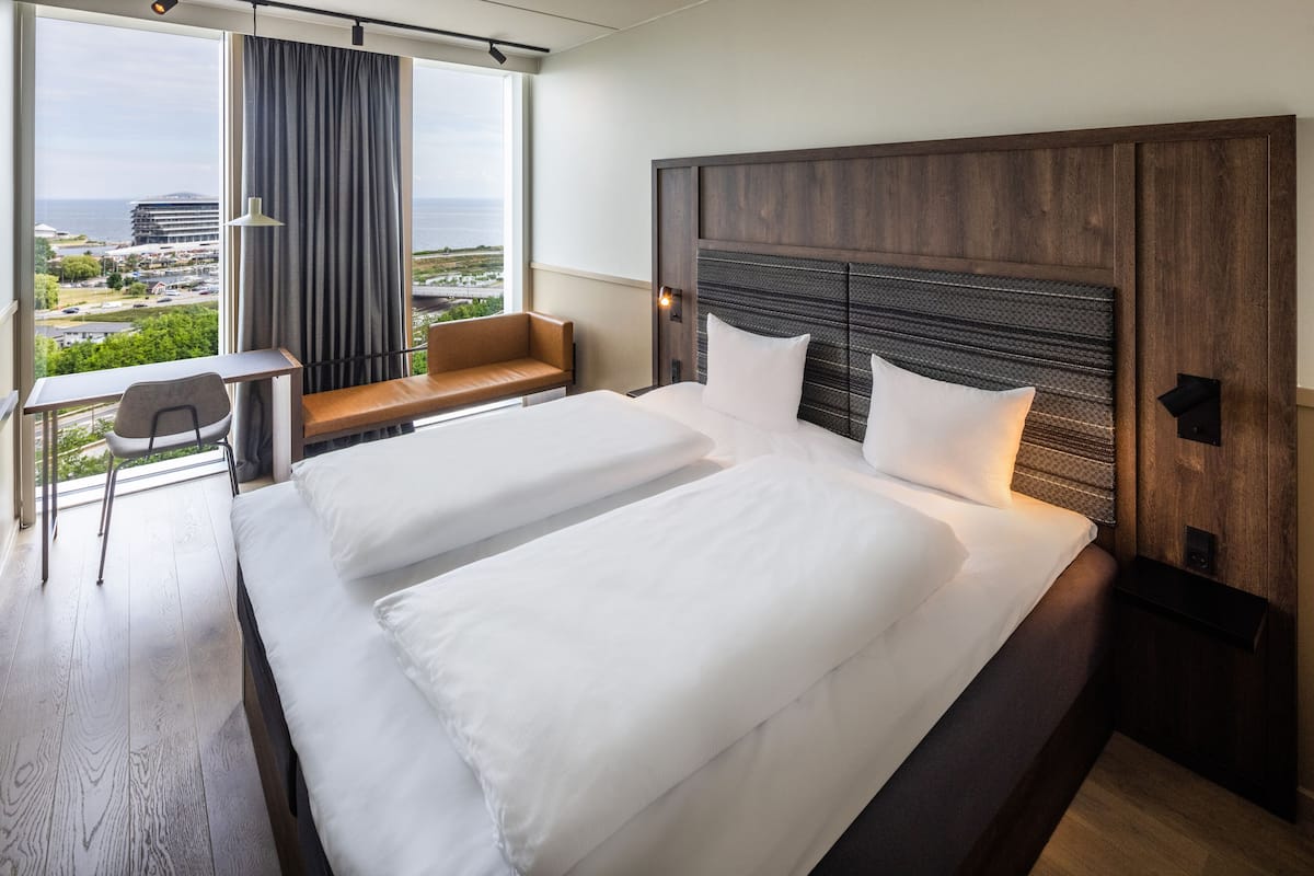 A hotel room with a large bed, a desk, a chair, and a view of the city and ocean.