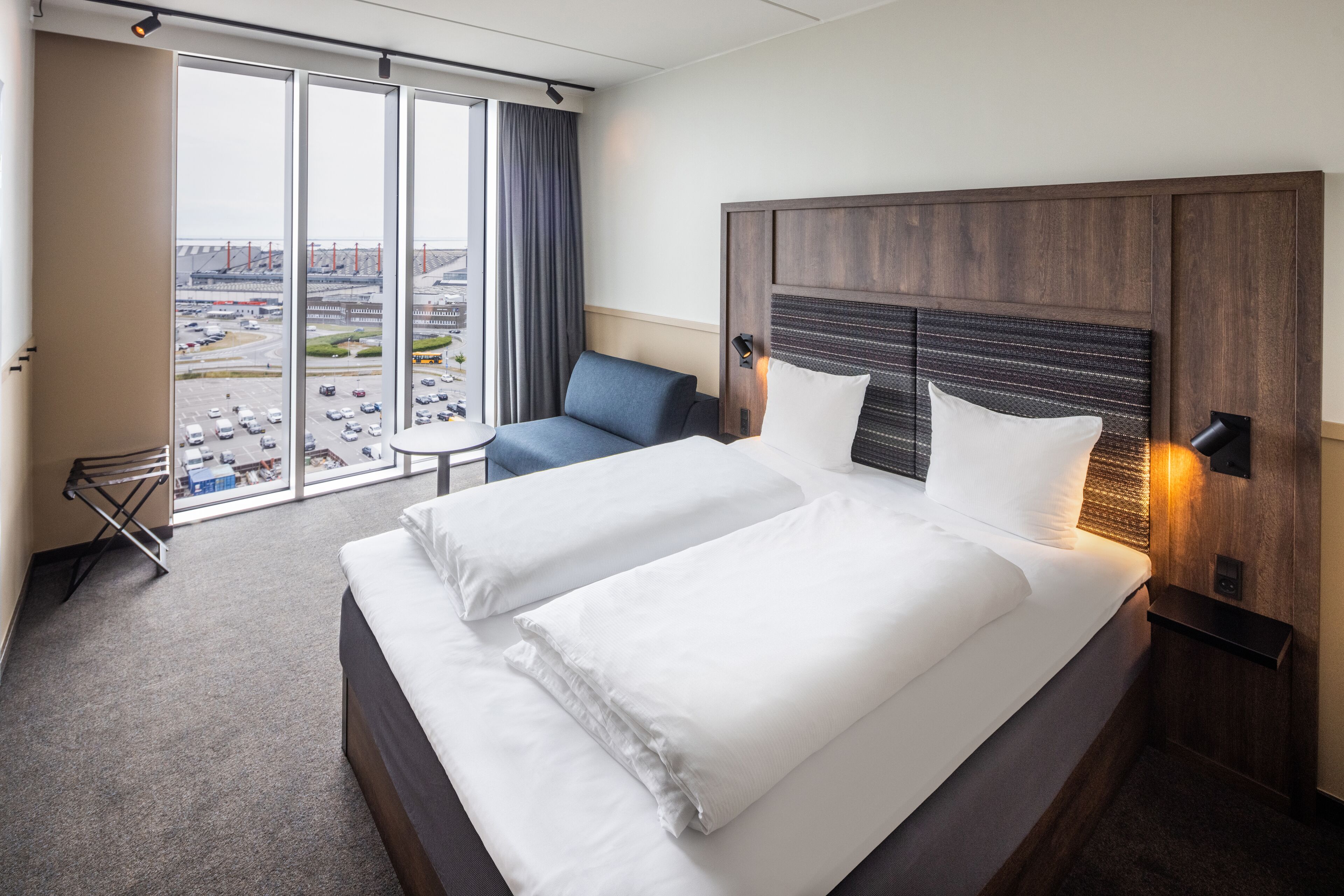 A hotel room with a large bed, a desk, and a view of the city through the window.