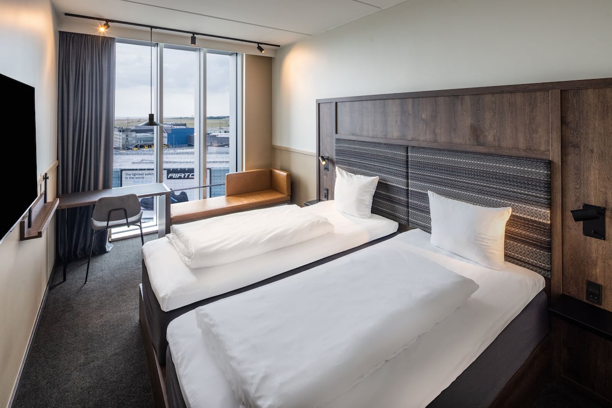 A hotel room with two beds, a desk, and a chair.