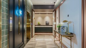 A hotel lobby with a reception desk, a console table with a lamp, and a geometric patterned floor. - Manxin Hotel Qingdao Zhanqiao (Qingdao)