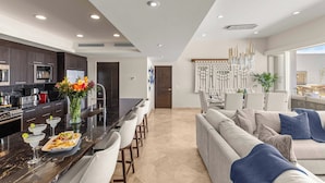 A modern kitchen with dark cabinets, a marble countertop, and a dining area with a sofa and chairs. - Luxury PH Cascadas in Cabo Central Location, Ocean Views, 5-Star Service (Pedregal)
