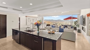 A modern kitchen with a large island, a dining area with a red umbrella, and a view of a cityscape. - Luxury PH Cascadas in Cabo Central Location, Ocean Views, 5-Star Service (Pedregal)