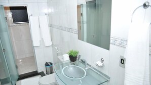 Ein modernes Badezimmer mit einem Waschbecken aus Glas, weißen Fliesen, einer Toilette und einer Duschkabine.