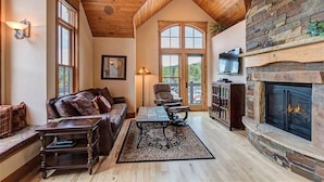 A cozy living room with a fireplace, wooden ceiling, and large windows.