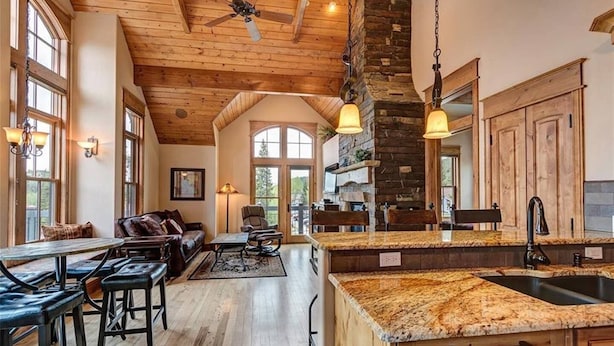A spacious kitchen with a stone fireplace, wooden ceiling, and large windows.