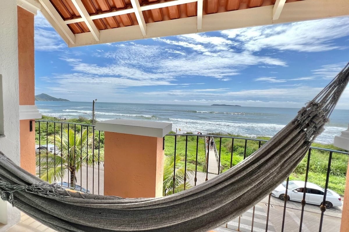 A hammock on a balcony overlooking the ocean with a clear view of the sea and distant land.