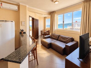 A modern living room with a sofa, a dining area, and a kitchen with a refrigerator. - Villa dos Açores Pousada (Bombinhas)