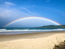 Uma praia com um arco-íris sobre o oceano e uma montanha ao longe.