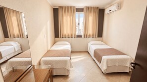 Habitación de hotel con dos camas individuales, un escritorio pequeño, un espejo y un equipo de aire acondicionado.