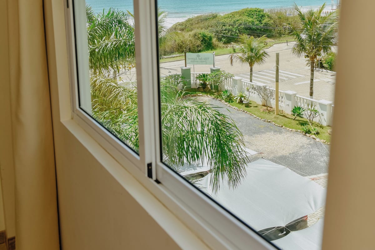A window with a view of a beach, palm trees, and a road.