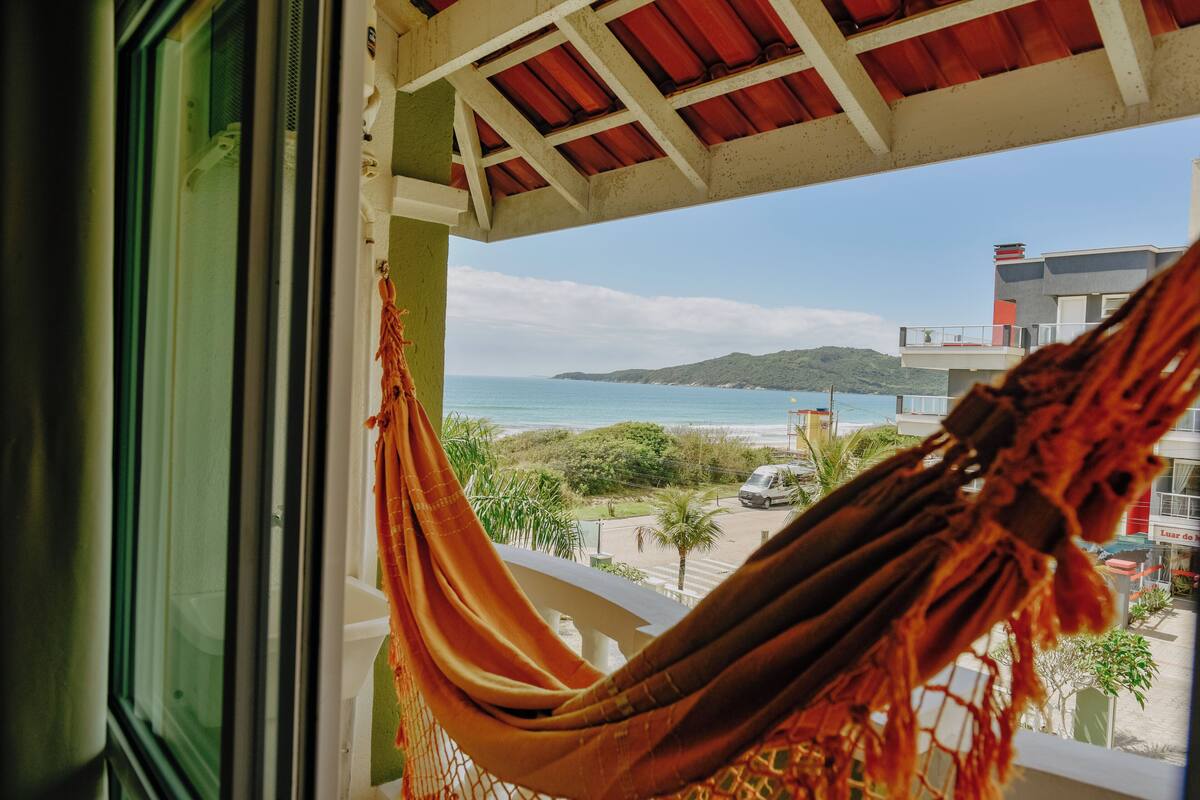 A window view of a beach with a hammock hanging inside.