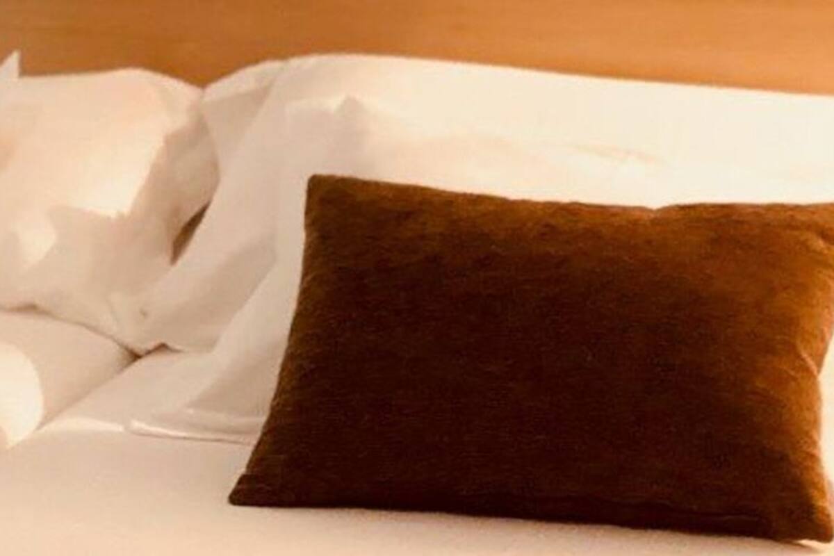A neatly made bed with white linens and two brown pillows.