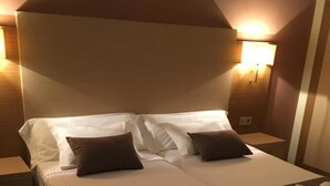 Une chambre d’hôtel avec deux lits, chacun recouvert de draps blancs et agrémenté d’oreillers marron, ainsi qu’une couverture marron et une petite table sur laquelle sont posés une serviette et une autre, enroulée.