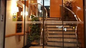 L’entrée d’un hôtel, avec une porte en verre, un escalier menant à l’intérieur et un panneau indiquant un délai d’enregistrement de 30 minutes.
