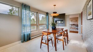 A modern dining area with a wooden table and chairs, a potted plant, and large windows with curtains. - Discovery Park House (Wheat Ridge)