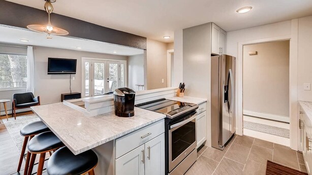 A modern kitchen with a central island, stainless steel appliances, and a dining area with bar stools. - Discovery Park House (Wheat Ridge)