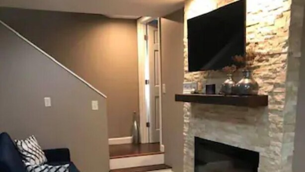 A living room with a stone fireplace, a mounted TV, and a staircase leading to another level.