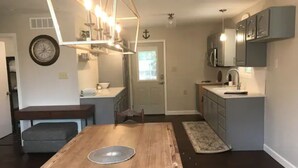 A modern kitchen with grey cabinets, a wooden dining table, and a chandelier.