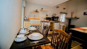 A dining area with a table set for four, a kitchen in the background, and a stone shelf with a vase. - Cozy Irish cottage, located on the Wild Atlantic Way! (Fanore)