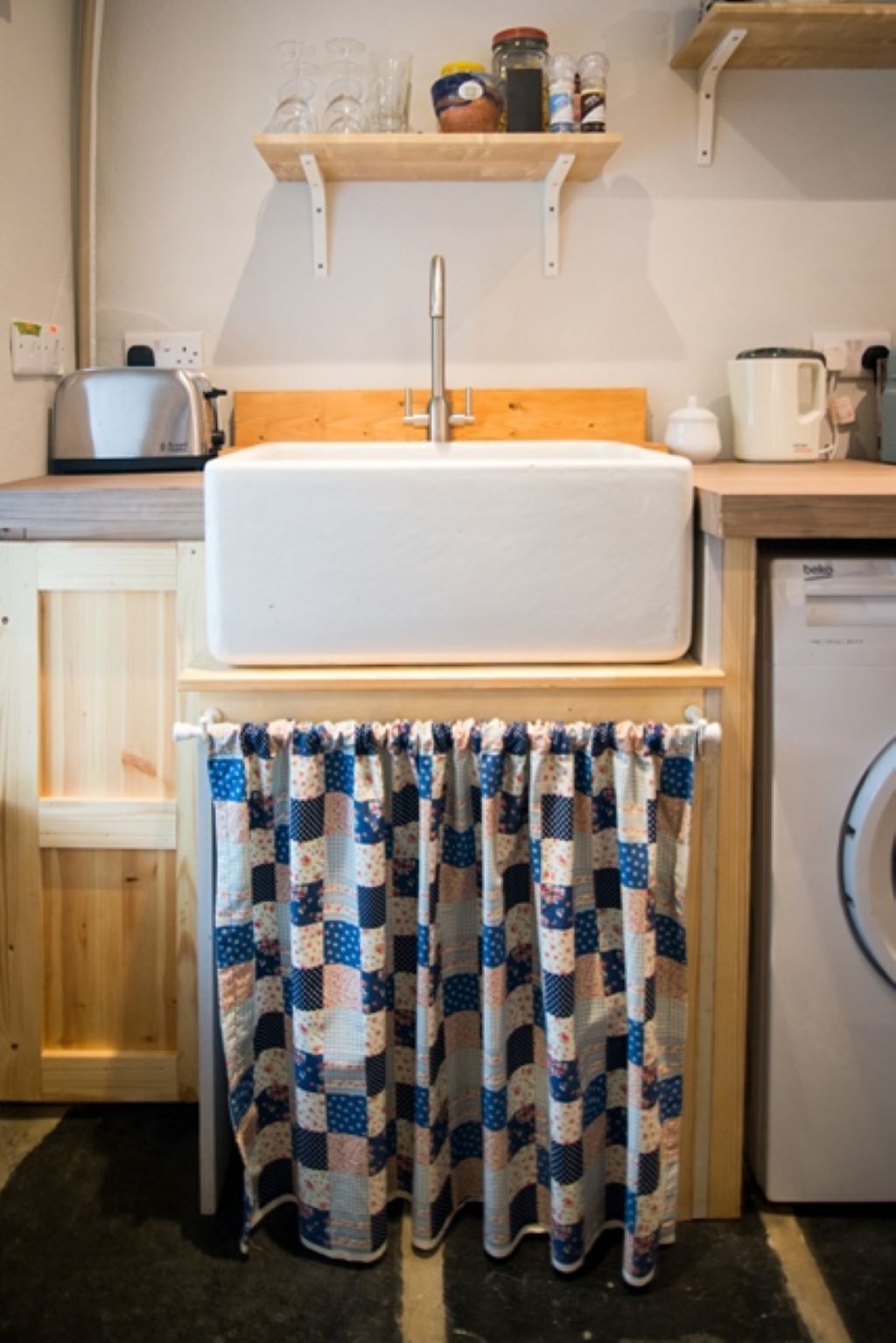 Une cuisine avec un évier blanc, des placards en bois, un plan de travail en bois et un lave-linge.